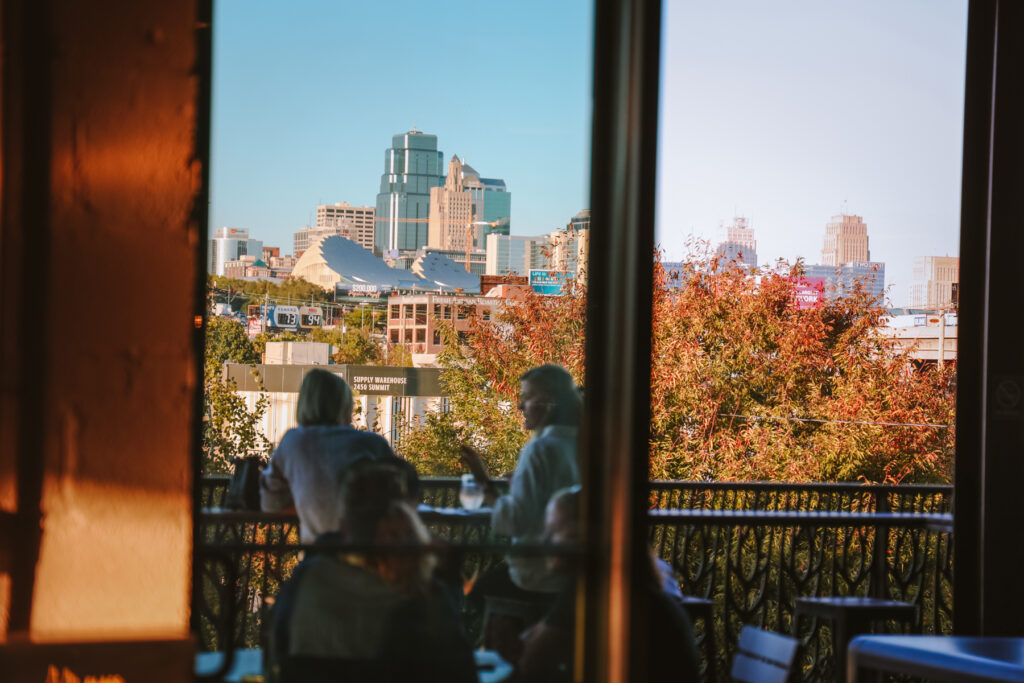 People sitting on the Boulevard Brewing Co. Beer Hall balcony overlooking the Kansas City skyline.
