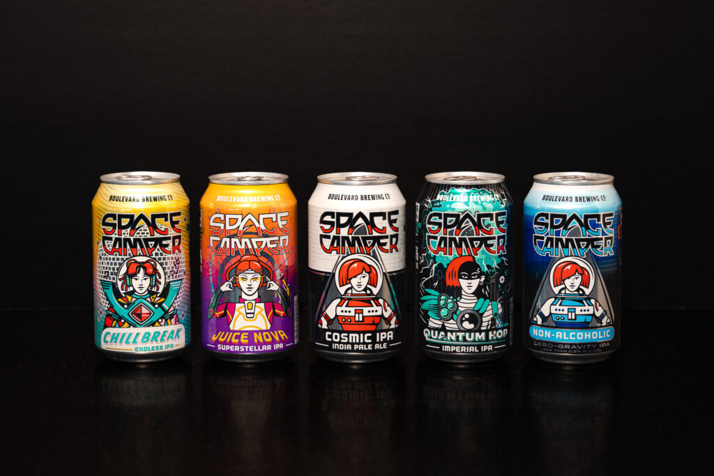 Five colorful Space Camper beer cans lined up against a black background, each featuring a cartoon astronaut and distinct label designs for different Space Camper beer varieties.