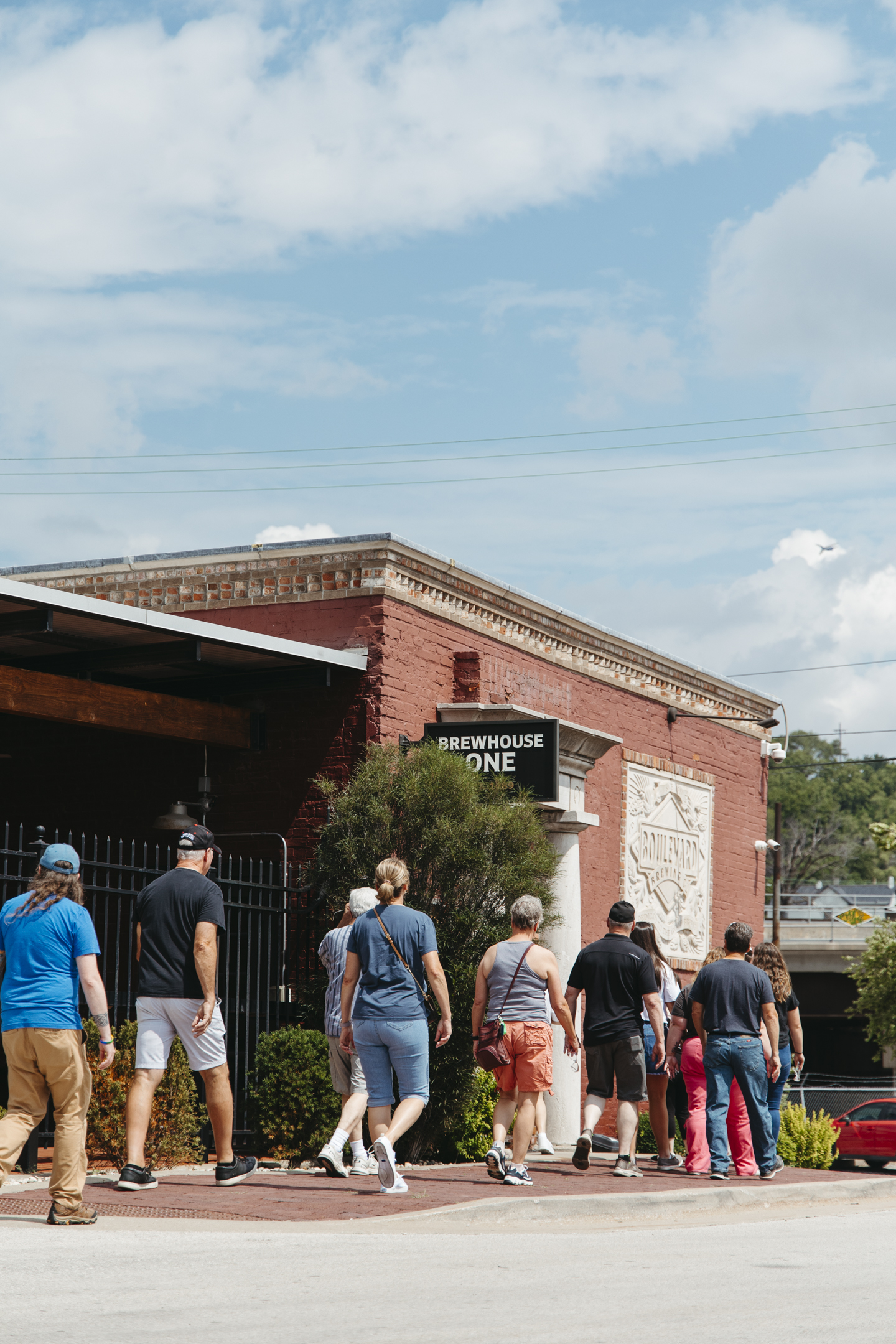 A group of people walks along a sidewalk toward the Boulevard Brewing Co. Tours entrance, marked by a “BREWHOUSE ONE” sign.