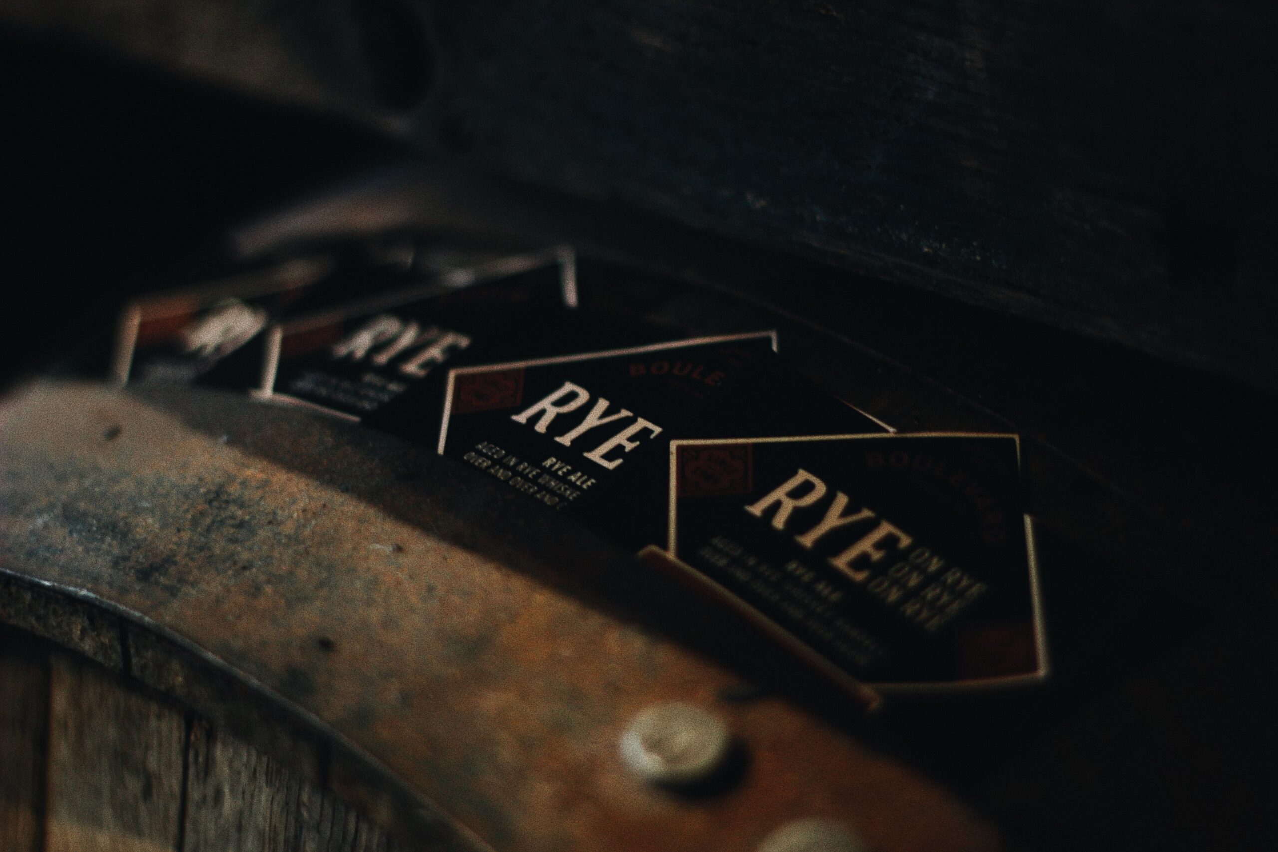 A moody, dimly lit image shows business cards with "RYE" prominently displayed. They are spread out on a wooden surface with an amber hue, creating an intimate, rustic atmosphere.