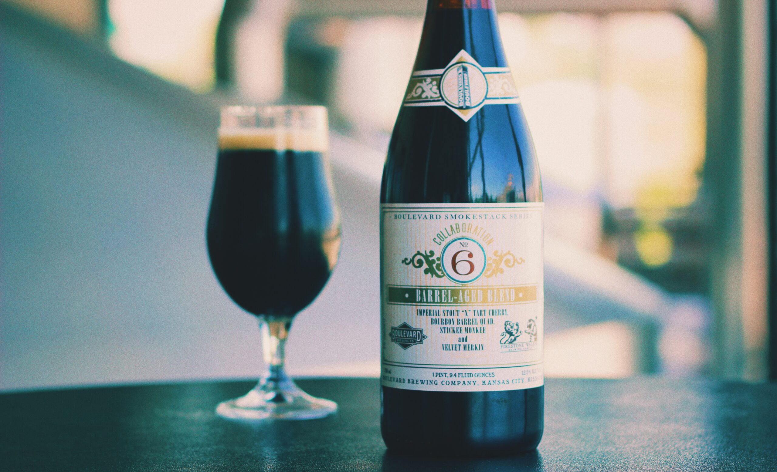 A bottle of Boulevard Brewing Co.'s Barrel-Aged Stout and a filled glass sit on a dark surface. The bottle has a detailed label with gold and white accents, while the glass contains a dark-colored beer with a creamy head.