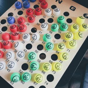 A vertical bingo card with transparent colored balls placed on it, each ball displaying a number between 1 and 75. The balls are organized by color: red, white, blue, green, and yellow, matching the columns headed by the letters B, I, N, G, and O.