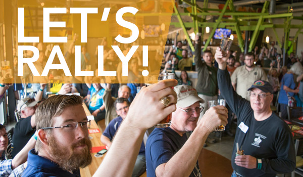 A crowd gathers in a lively indoor setting, raising glasses in celebration. The image features diverse people, with some standing and others seated, surrounded by bright decor. Large text overlay reads "LET'S RALLY!.