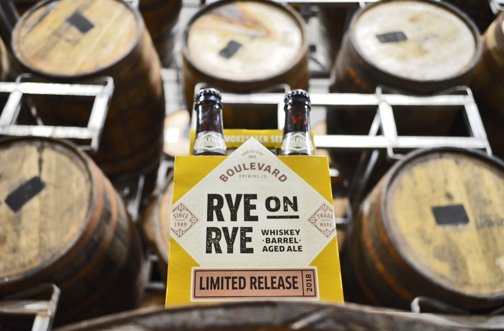 Pack of Boulevard Brewing Co.'s "Rye on Rye" whiskey-barrel aged ale in front of stacked wooden barrels. The packaging features a limited release label.
