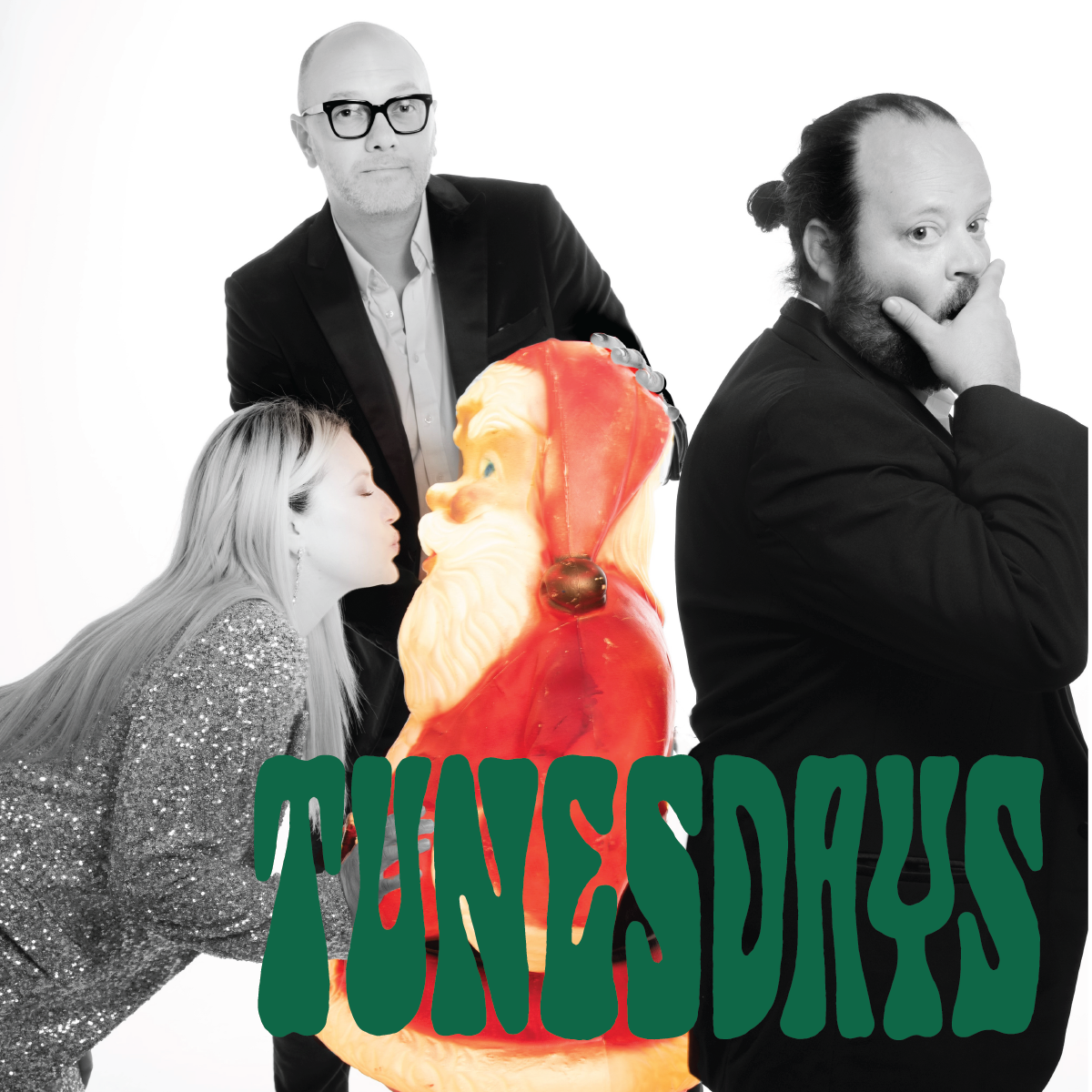 A group photo featuring three people around a large Santa Claus figurine, with "TUNESDAYS" written in large green curvy text at the bottom. One person is leaning in to kiss the Santa, another stands pensively, and the third person stands confidently with sunglasses.