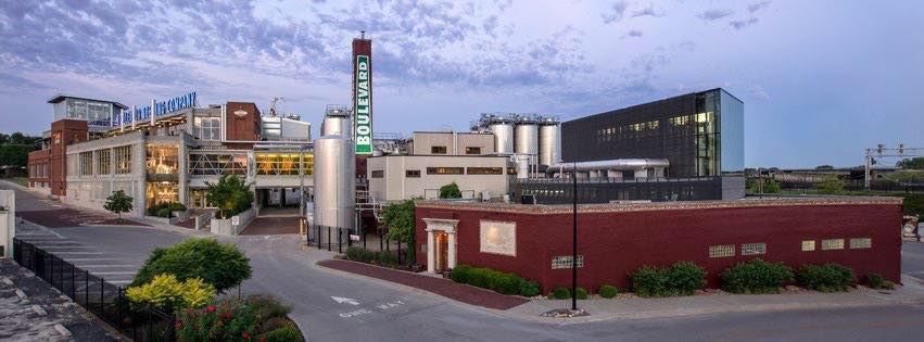 Panoramic view of an industrial brewery complex with multiple brick and metal buildings. Prominent signage reads "Boulevard." The complex includes large tanks and modern structures, set against a cloudy sky.