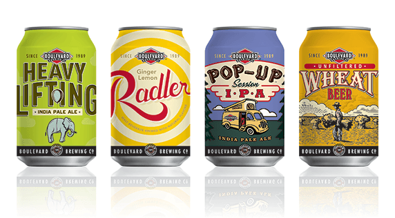 Four Boulevard Brewing Co. beer cans lined up. From left to right: Heavy Lifting IPA with an elephant design, Ginger Lemon Radler with a citrus swirl, Pop-Up Session IPA with a camping scene, and Unfiltered Wheat Beer with a farmer and field.