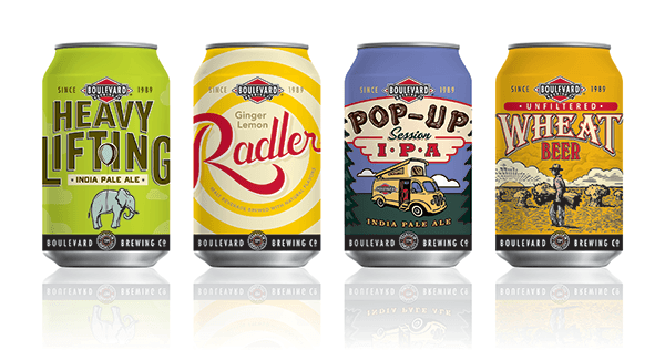 Four Boulevard Brewing Co. beer cans lined up. From left to right: Heavy Lifting IPA with an elephant design, Ginger Lemon Radler with a citrus swirl, Pop-Up Session IPA with a camping scene, and Unfiltered Wheat Beer with a farmer and field.