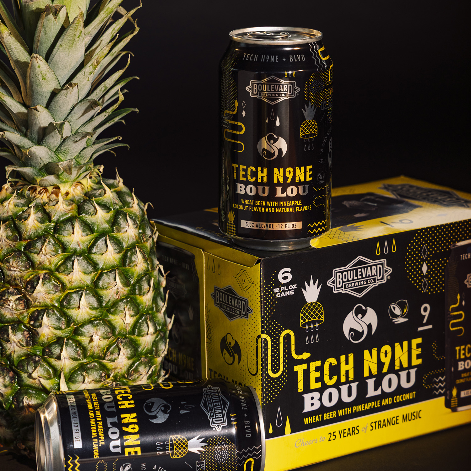 A fresh pineapple sits next to a six-pack of Boulevard Brewing Co.'s Tech N9ne Bou Lou wheat beer; one can is upright and another lies sideways, both featuring black and gold designs.