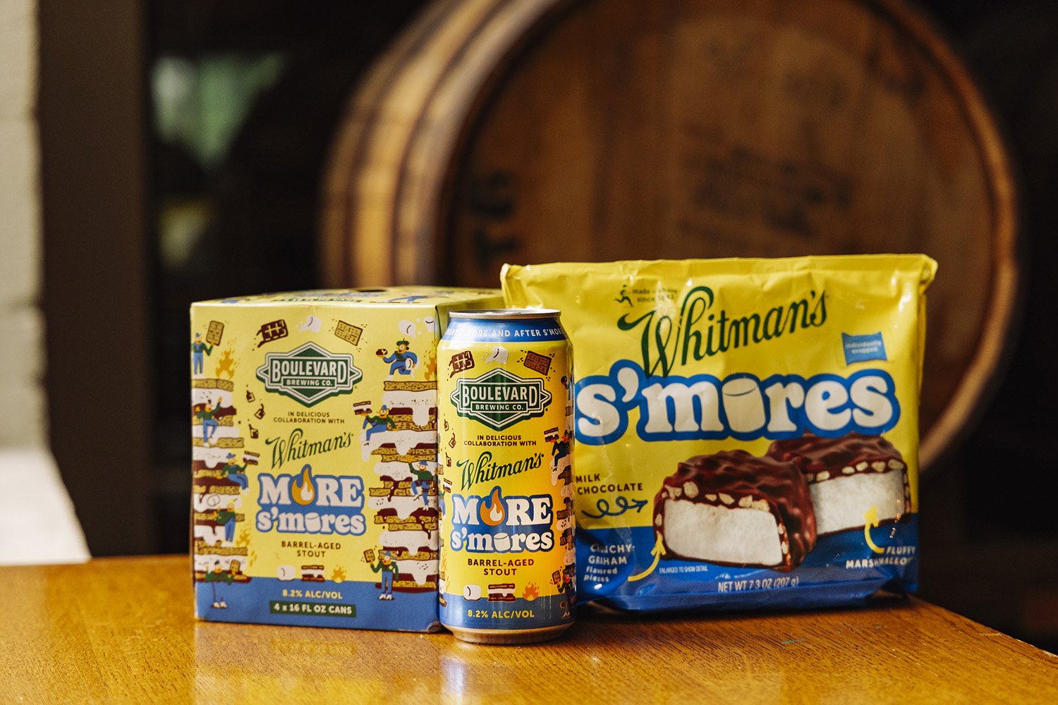A can and pack of Boulevard Brewing Co.'s More S'mores stout sit next to a package of Whitman's S'mores chocolate-covered marshmallow treats on a wooden table, with a barrel in the background.