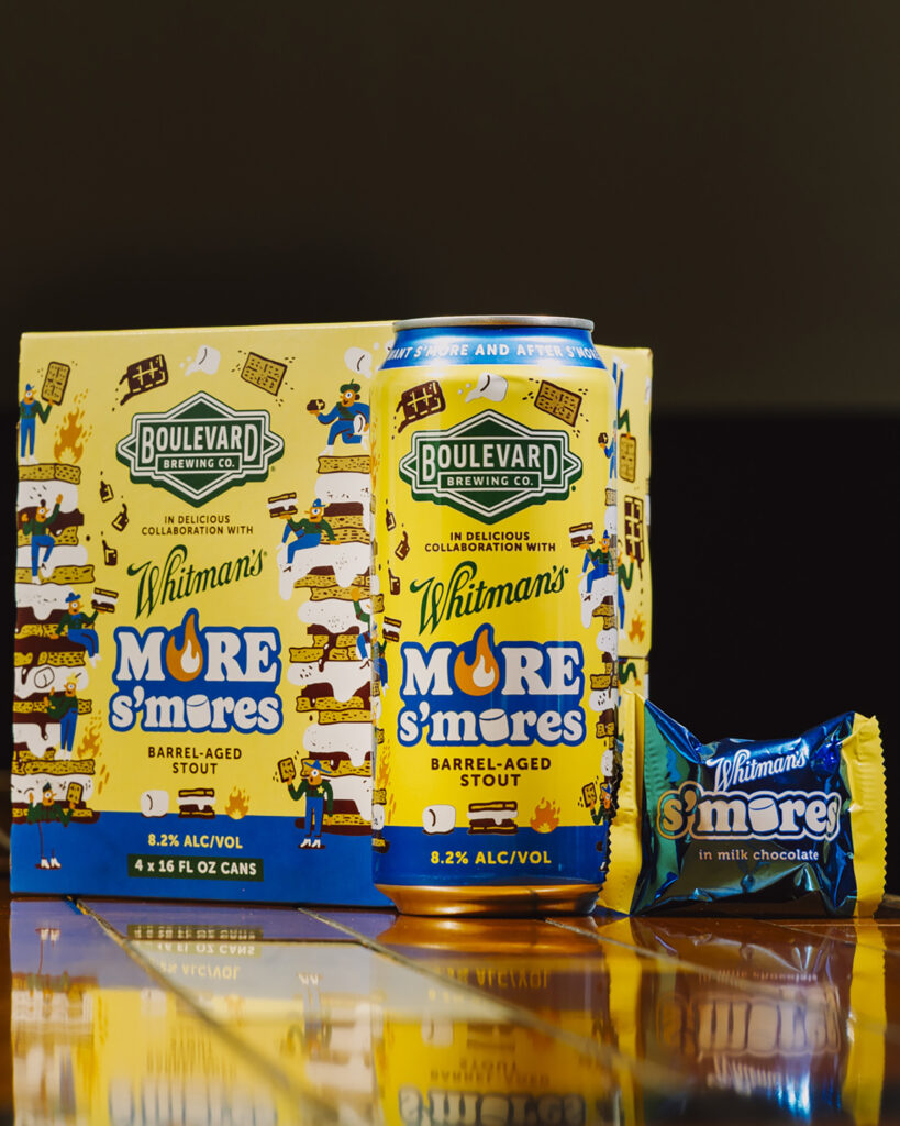 A box, can, and chocolate bar of Boulevard Brewing Co.'s More S'mores Whitman's Barrel-Aged Stout are displayed on a reflective surface. The yellow packaging features playful illustrations with blue, white, and brown text.