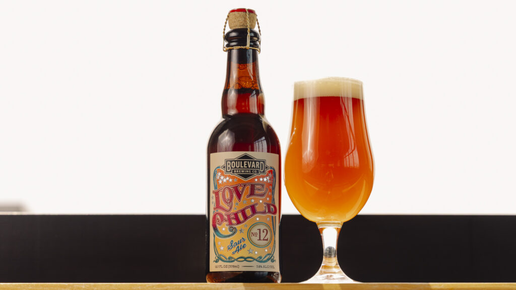 A bottle of Boulevard Love Child No. 12 beer with a colorful label stands next to a filled tulip glass of amber beer with a foamy head, set against a light background—perfect for fans of the celebrated Love Child No. 10 series.