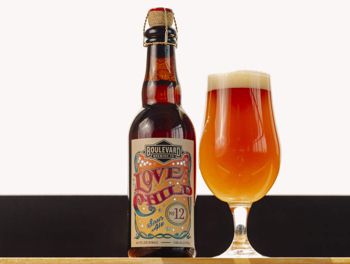 A bottle of Boulevard Love Child No. 12 beer with a colorful label stands next to a filled tulip glass of amber beer with a foamy head, set against a light background—perfect for fans of the celebrated Love Child No. 10 series.