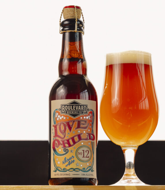 A bottle of Boulevard Love Child No. 12 beer with a colorful label stands next to a filled tulip glass of amber beer with a foamy head, set against a light background—perfect for fans of the celebrated Love Child No. 10 series.