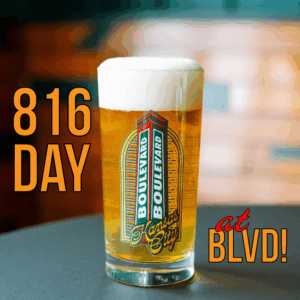 A pint glass of beer with a thick foam head sits on a table. The glass features the Boulevard Brewing Co. Kansas City logo. Text reads: “816 Day at BLVD!” in bold orange and red letters.