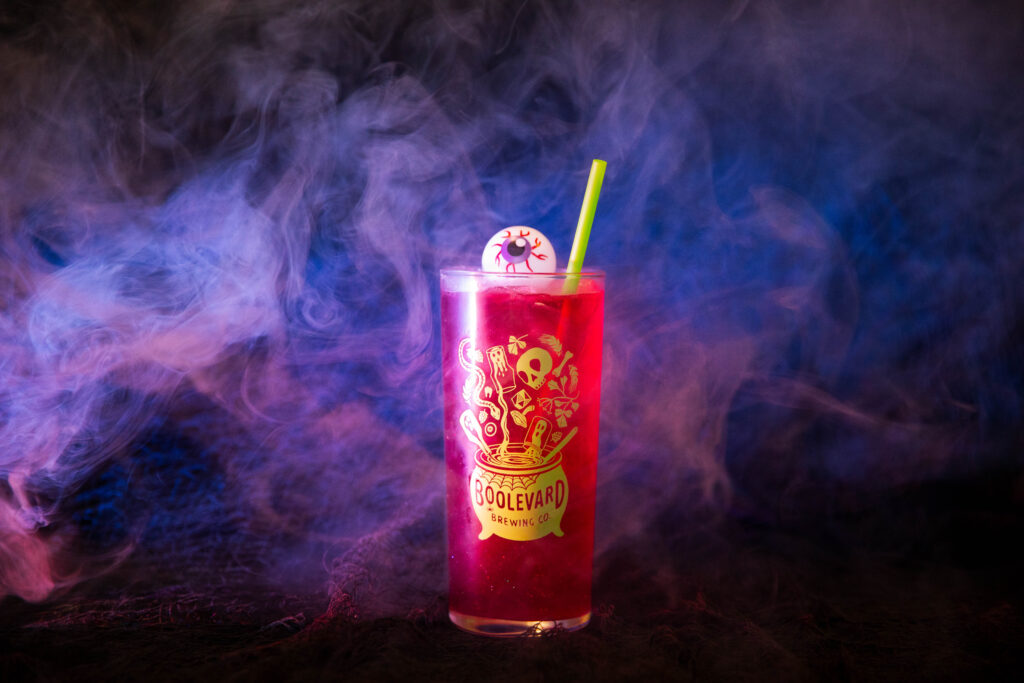 A tall glass of bright red Rec Deck the Halls drink with a green straw and a floating fake eyeball, set against a smoky, colorful background with the “Boulevard Brewing Co.” logo on the glass.