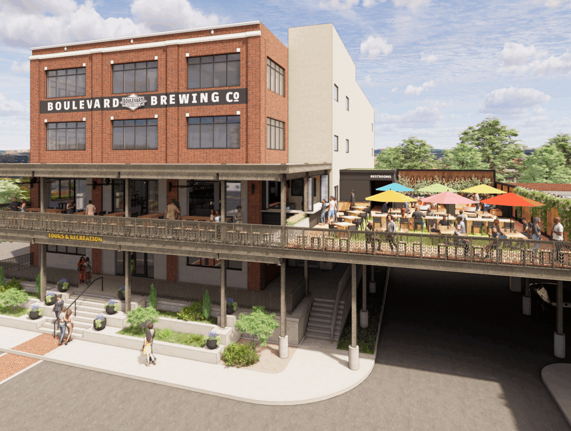 A brick building with a sign that reads "Boulevard Brewing Co" and “Brewhouse One,” featuring a large outdoor patio with colorful umbrellas, tables, and people; trees and parked cars are visible in the background.