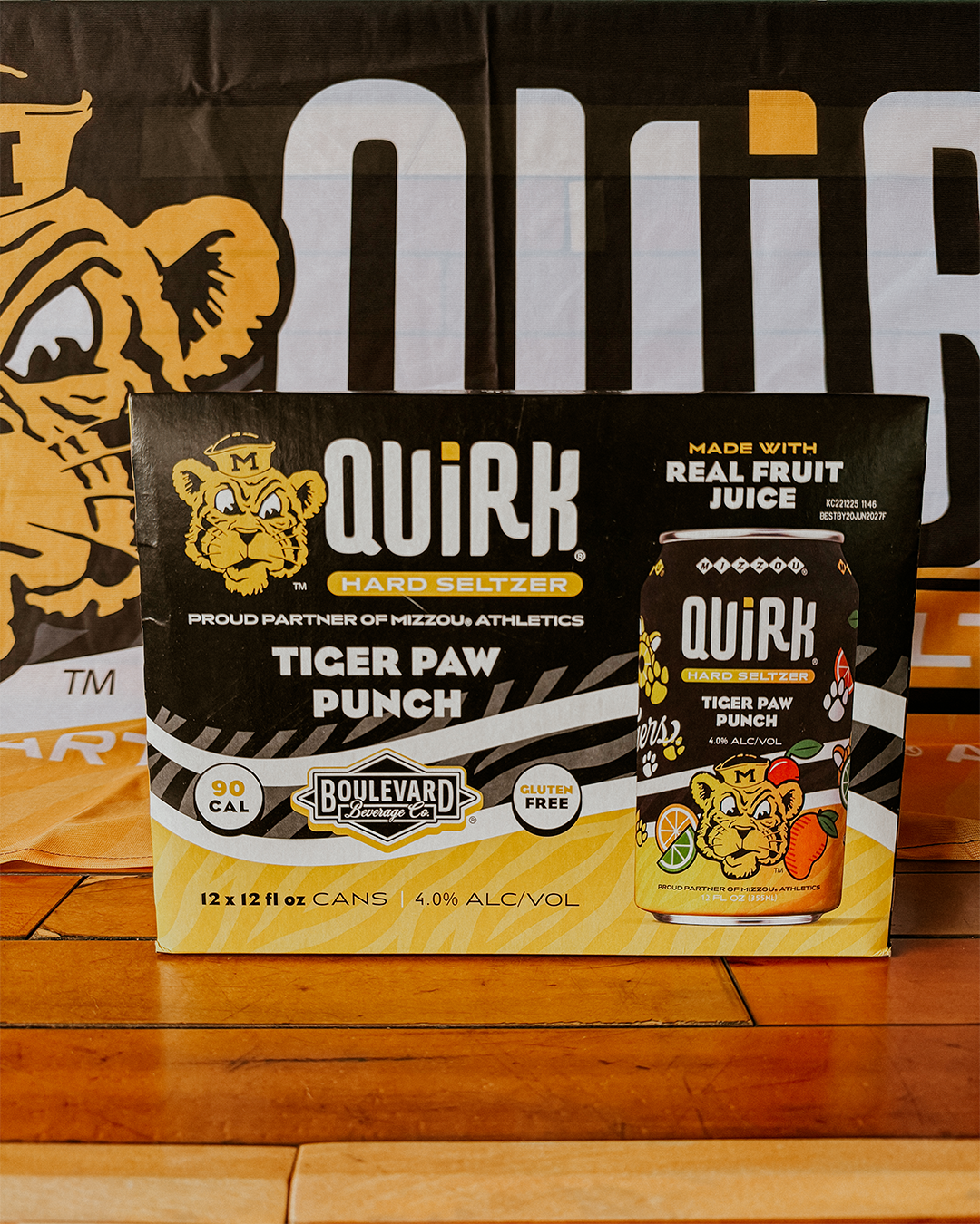 A 12-pack box of Quirk Hard Seltzer Tiger Paw Punch, featuring a can with a tiger mascot and fruit illustrations. The box states it has 90 calories, is gluten free, and made with real fruit juice.