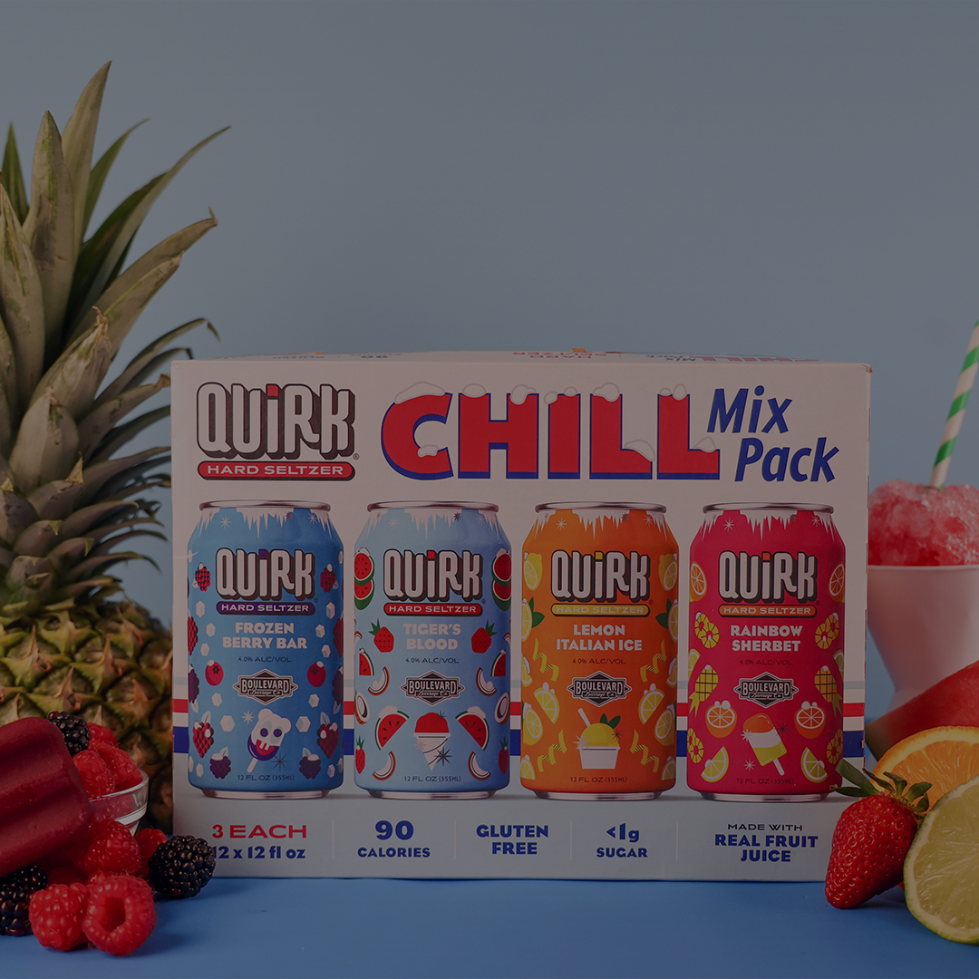 A box of Boulevard Brewing Co. Quirk Chill Mix Pack hard seltzers from Kansas City, Missouri, is displayed with four cans in fun flavors: Frozen Berry Bar, Tiger’s Blood, Lemon Italian Ice, and Rainbow Sherbet. Fruits and a pineapple surround the box.