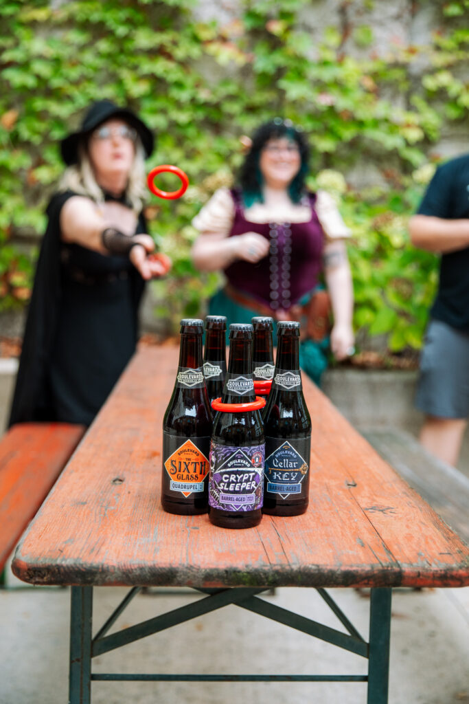 A ring-toss game being played with Boulevard beer bottles on a wooden picnic table.