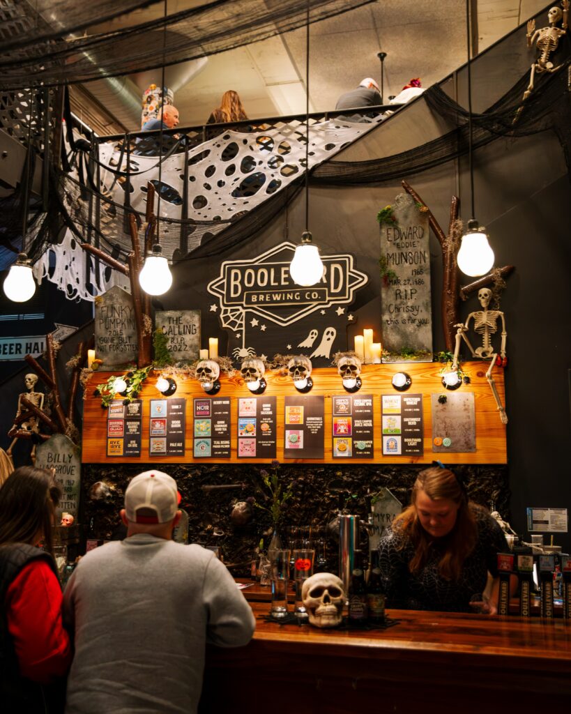 A brewery taproom decorated for Halloween features a menu board with a list of beers, skeletons, and a Boulevard Brewing Co. sign hanging above the bar.